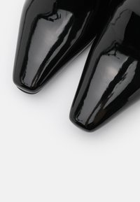 Escarpins à talons hauts en cuir verni noir avec un design à bout pointu, présentant une finition brillante et une texture lisse.