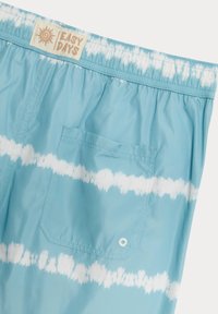 Bañador de tie-dye azul hecho de material ligero. Cuenta con una cinturilla elástica, un bolsillo trasero y franjas onduladas blancas. Etiqueta de Easy Days visible.