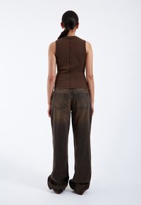 Débardeur marron à côtes associé à un jean large marron délavé. Le débardeur possède une couture droite dans le dos ; le jean a deux poches arrière.