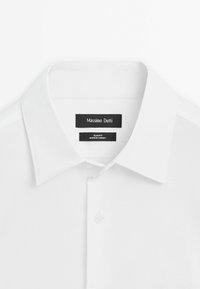 White dress shirt with spread collar, one visible button, and black tags labeled Massimo Dutti and slim fit, made in Turkey.