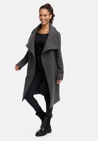 Grå kappa med stor krage, tillverkad av mjukt material. Matchad med svart topp och slim fit jeans. Svarta ankelboots fulländar outfiten.