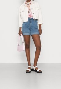 Vit kort denimjacka, blommig topp, höga blå denimshorts, rosa handväska och svarta platåsandaler med vita remmar.