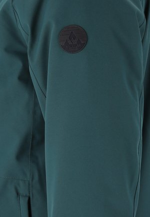 Dark green jacket sleeve with black circular patch featuring mountain logo and "WHISTLER" text on upper arm.