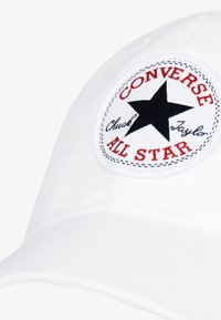 Gorra de béisbol blanca con un logo redondo de Converse All Star en negro y rojo que presenta una estrella negra y texto bordado. Textura de tela suave.