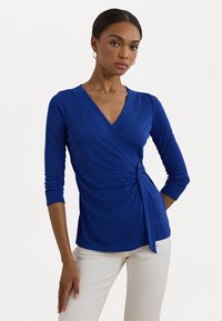 Royal blue, long-sleeve wrap top with a V-neck and gathered side detail. Made from soft fabric, featuring a knot accent at the waist.