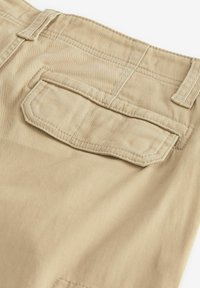 Pantaloni din bumbac bej cu un buzunar posterior ce dispune de o clapetă, accente de cusătură și o textură netedă. Include talie ajustabilă.