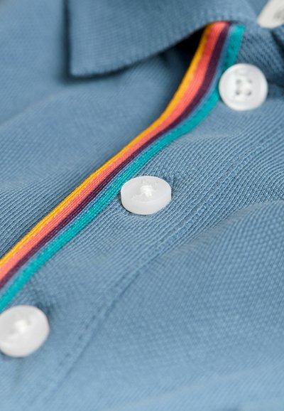 Šviesiai mėlynas marškinis, pasižymintis tekstūruotu audiniu, su apykakle, papuošta daugiaspalve dryžuota juostele ir baltais plastikininiais mygtukais.