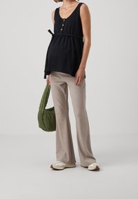 Haut sans manches noir avec un décolleté en V et des boutons, associé à un pantalon beige évasé et un sac matelassé vert. Les chaussures présentent des accents clairs et sombres.