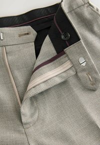 Gray woven trousers featuring a black waistband, contrasting inner lining, a zipped pocket, and metallic hardware accents.