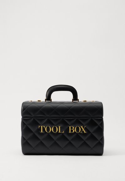 Černá prošívaná taška na nářadí s zlatým nápisem "TOOL BOX", strukturovaný tvar, horní úchyt a zlaté kovové detaily.