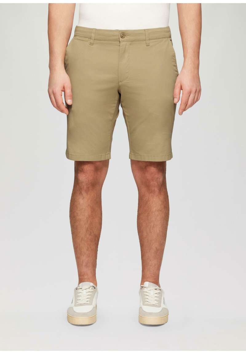 Khaki-shortsit, joissa on suora leikkaus, valmistettu kevyestä kankaasta, jossa on kaksi sivutaskua ja nappikiinnitys. Yhdistetty valkoisiin lenkkareihin.