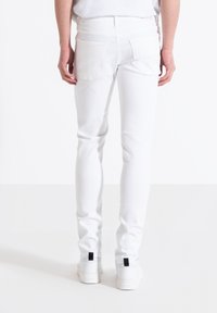 Jeans de mezclilla blancos con un corte ajustado, con cinco bolsillos y una cintura clásica. Las piernas son ajustadas, con una textura suave y sin patrones visibles.