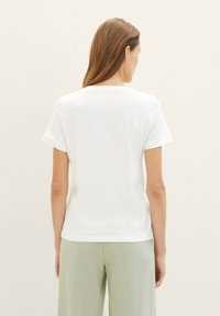 Witte T-shirt met korte mouwen en een ronde hals, met een gladde, zachte textuur, gezien van achteren, gecombineerd met lichtgroene broek.
