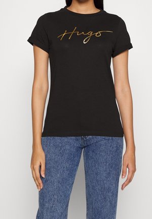 Zwarte katoenen t-shirt met opgerolde mouwen, met een gouden schriftontwerp dat "Hugs" over de borst leest. Standaard pasvorm en ronde hals.