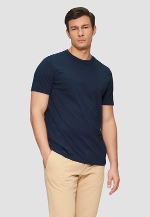 Marineblauwe katoenen t-shirt met een ronde halslijn en korte mouwen, voorzien van een subtiele logo op de linkerborst, gecombineerd met lichtbeige broek.