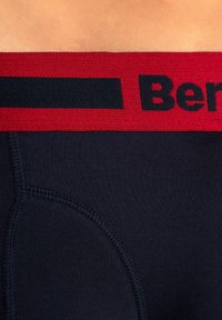 Temno modri boksarji z rdečim elastičnim pasom, na katerem je črn logotip. Tkanina je gladka, z vgrajenim šivom ob strani.