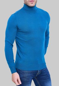 Un pull à col roulé bleu épais, à texture côtelée, avec une coupe ajustée et des manches longues, de couleur unie, assorti à un jean foncé.