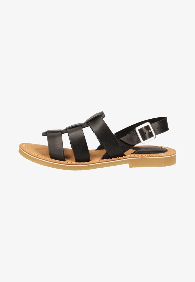 Sandale plate en cuir noir avec trois lanières sur le dessus du pied et une lanière avec boucle réglable autour de la cheville, sur une semelle couleur fauve.