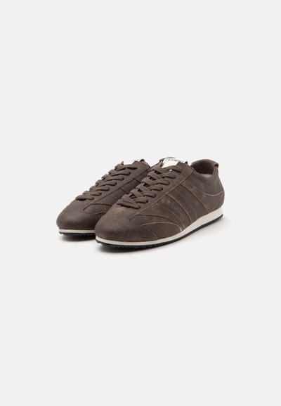 Paire de baskets en daim marron foncé avec semelles blanches et lacets marron assortis sur fond gris clair.
