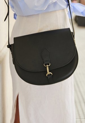 Schwarze Leder-Crossbody-Tasche mit abgerundetem Deckel, goldener Hardware und einem langen Tragegurt. Verfügt über ein dezentes geprägtes Detail auf dem Deckel.