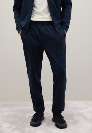 Marine blauwe sport joggers met een elastische tailleband en zijzakken, gemaakt van gladde, rekbare stof, gecombineerd met zwarte sportschoenen.
