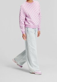 Ljusrosa sweatshirt med vitt blixtmönster, kombinerad med vida ljusblå jeans och sneakers med lila detaljer.