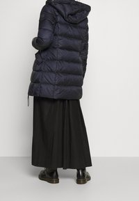 Navy pufferjas met een capuchon, horizontaal gestikte ontwerpen en een langere lengte. Gepaard met een zwarte maxi-rok en zwarte laarzen.