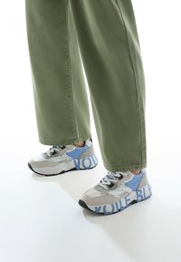 Sneaker mit einem Farbdesign in Grau, Blau und Weiß; Gummisohle; große bedruckte Schriftzüge an der Seite; Materialien aus Stoff und Wildleder.