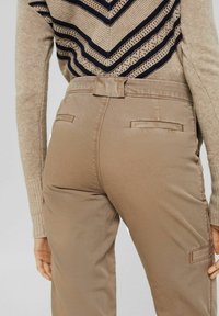 Beige byxor med slim fit, featuring en platt midjeband och bakfickor. Tyget är slätt med en lätt lyster.