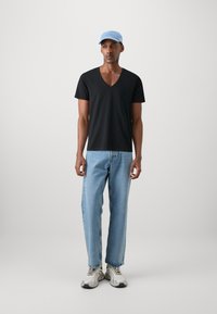 Tricou negru cu guler în V, capac bleu deschis, blugi bleu deschis și adidași gri cu accente galbene. Design simplu, casual și potrivire confortabilă.