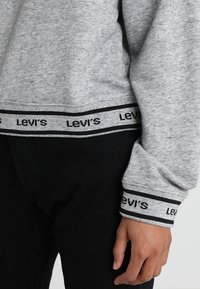 Felpa grigia con polsini a coste con logo "Levi's" in bianco e nero, realizzata in tessuto morbido, abbinata a pantaloni neri.