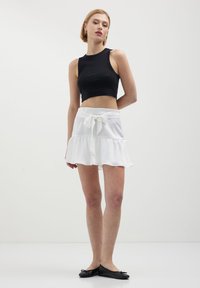 Top corto nero con scollo rotondo, abbinato a una minigonna bianca con vita annodata e volants sovrapposti. Scarpe flat nere.