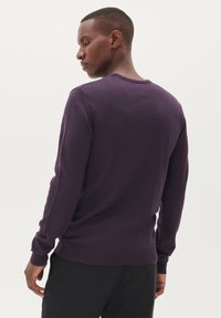 Ljubičasti pulover s okruglim izrezom, dugim rukavima i rebrastim manžetama i rubom. Čini se da je materijal pleten i teksturiran. Nositi se s tamnim hlačama.