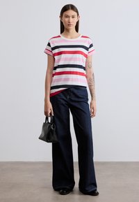 Ριγέ κοντομάνικη μπλούζα σε ροζ, κόκκινο, ναυτικό μπλε και άσπρο, συνδυασμένη με φαρδιά τζιν παντελόνια σκούρου χρώματος. Μαύρη τσάντα χειρός με χερούλια πάνω.