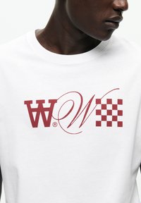 Tricou alb din bumbac cu logo imprimat maron cu litere stilizate și model carourile. Gât rotund și croială standard.