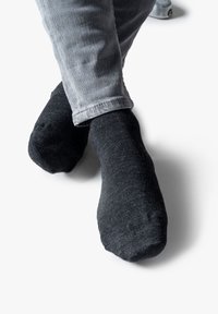 Schwarze Baumwollsocken mit glatter Textur, ausgestattet mit verstärkten Zehen. Getragen mit hellgrauen Hosen, die den Knöchelbereich zeigen.