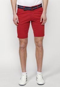 Shorts en coton rouge avec des ourlets retroussés, dot�és d'une ceinture rayée marine. Associés à des baskets blanches et un t-shirt blanc.