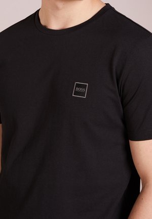 Schwarzes Baumwoll-T-Shirt mit Rundhalsausschnitt und kurzen Ärmeln, das ein kleines quadratisches Logo auf der linken Brustseite zeigt. Weicher Stoff.
