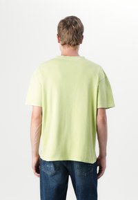 Light green short-sleeve t-shirt with a round neckline, made of soft fabric; displayed from the back, features a relaxed fit.