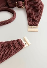 Barna, texturált szövetből készült bikini felső arany tónusú fém csattal és állítható pánttal, világos felületen.