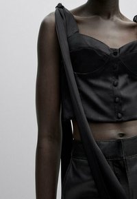 Black satin cropped top with a structured neckline, featuring buttons down the front and wide shoulder straps. Smooth texture and fitted design.