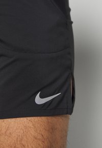 Pantalones cortos deportivos negros de tejido suave, con un logo gris de Nike cerca del dobladillo y aberturas laterales para mayor movilidad.