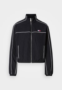 Μαύρο κοντό μπουφάν με λευκές ραφές, διαθέτει ψηλό γιακά, φερμουάρ μπροστά και μικρό λογότυπο στο στήθος. Κατασκευασμένο από ελαφρύ ύφασμα.