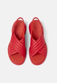 Sandalias rojas con un diseño entrelazado, confeccionadas en material sintético suave, con un acento decorativo redondo y abiertas por detrás.