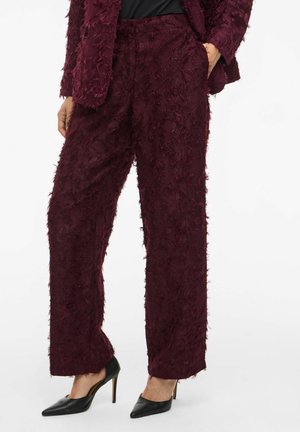 Pantalons larges bordeaux en tissu texturé avec des bords effilochés. Associés à des talons aiguilles noirs pour compléter le look.