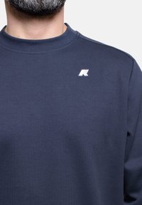 Felpa navy con collo a giro e polsini a costine. Presenta un piccolo logo bianco sul petto. Tessuto morbido e texture con vestibilità rilassata.