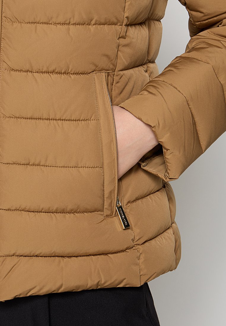 Braune Puffjacke mit gestepptem Design, Seitentaschen und einem leichten Glanz. Das Material wirkt glatt und isoliert, um Wärme zu bieten.