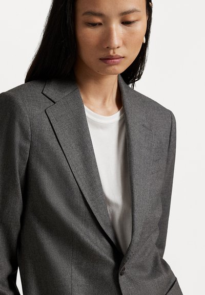 Siv blazer s prilagojenim krojem z izrezanim ovratnikom, enojnim gumbom in strukturiranim krojem, oblečen čez belo srajco. Gladek, teksturiran material.
