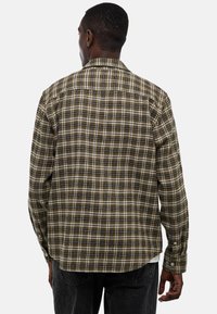 Chemise à carreaux marron et crème avec manches longues, présentant des motifs à carreaux contrastants et un col classique.