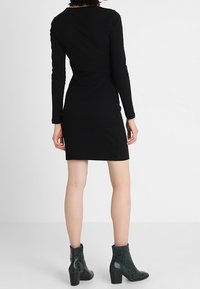 Czarna, prążkowana sukienka z długimi rękawami, dopasowany krój, długość do kolan. Noszona z zielonymi botkami za kostkę o fakturowanej powierzchni i słupkowym obcasie.